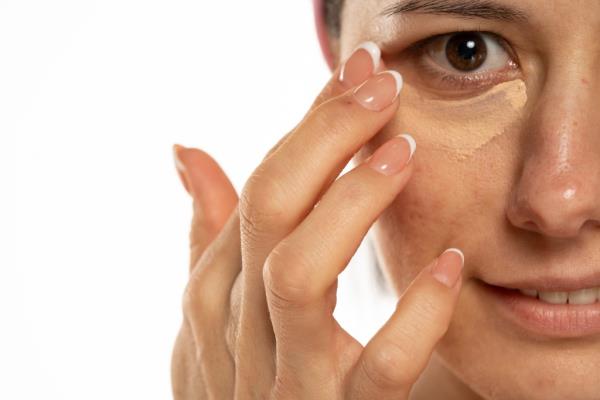 Middle-aged woman applying concealer under her eye on a white background